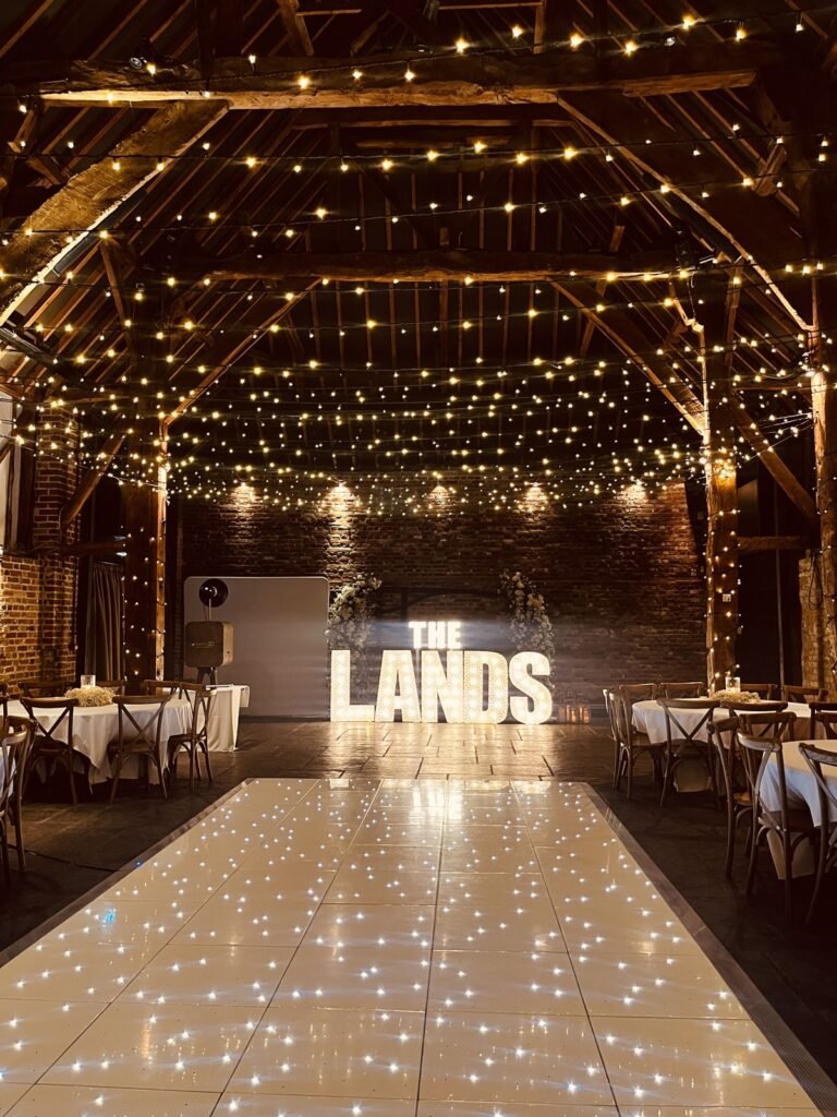 White LED dance floor and illuminated surname under fairy lights at Cooling Castle Barn