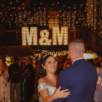Couple sharing their first dance under illuminated M&M letters as guests watch